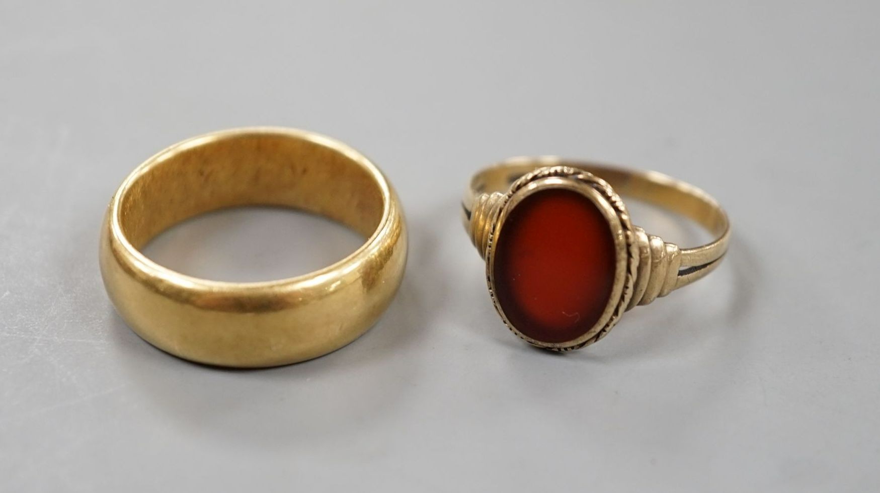 A George V 18ct gold wedding band, size Q, 14 grams and a 333 standard yellow metal and carnelian set signet ring, size R, gross weight 2.8 grams.